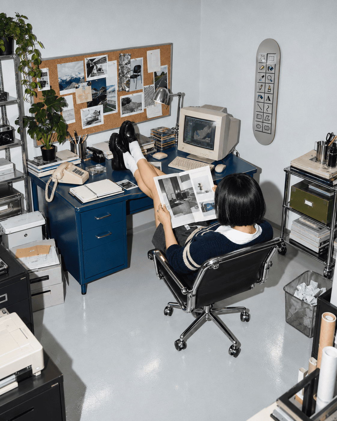 Retro pixel art skateboard wall art on the wall of a 90s-style office with a blue metal desk, beige CRT computer, cork board and chrome chair