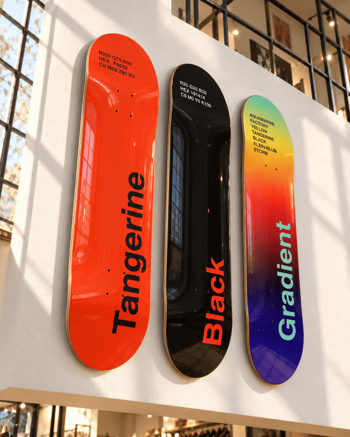 Three DeckArts skateboard decks in Tangerine, Black and Gradient hung in a row on a white loft wall