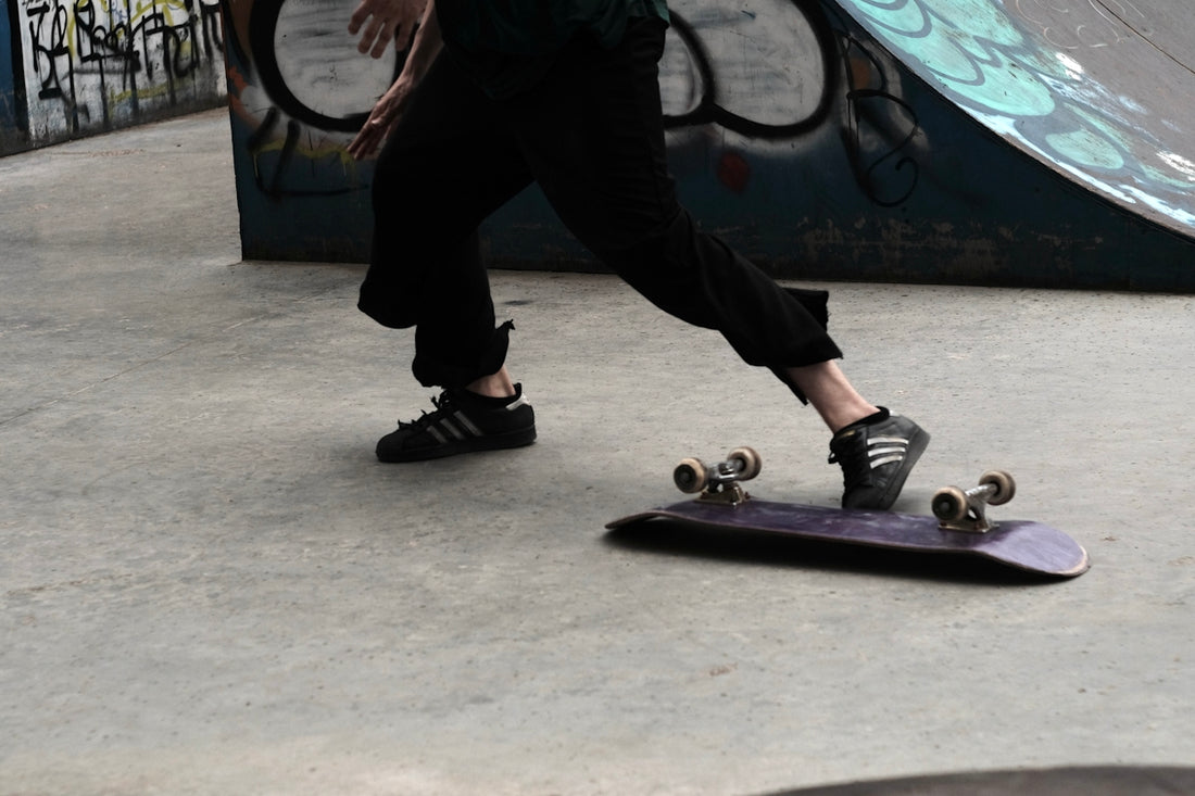 person in black pants and white sneakers standing on purple skateboard