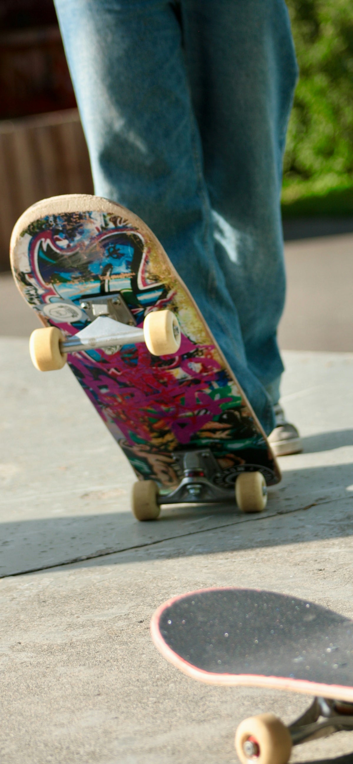 A person stands near a colorful skateboard on concrete.