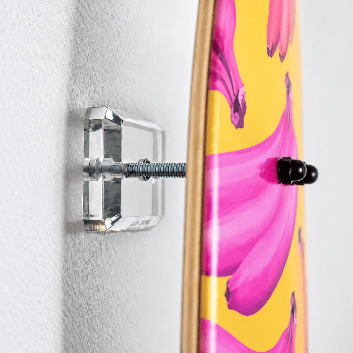 Side view of a clear acrylic skateboard wall mount on a white wall, steel rod holding a banana-art deck off the wall